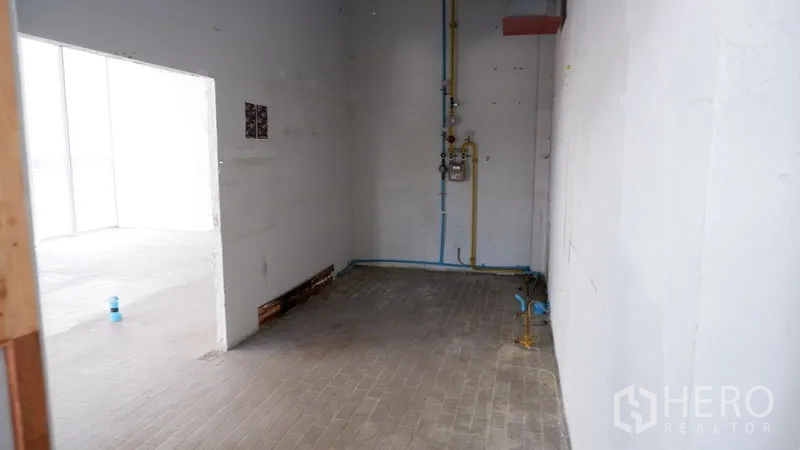 零售空间 出租在Watthana, Bangkok - 后勤区带管线与白色墙面，通向主营业空间的门洞。