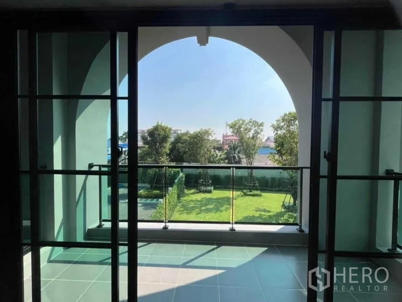 Detached House for sale in Mueang Nonthaburi, Nonthaburi - Covered balcony with arched opening and glass railing overlooking the garden.