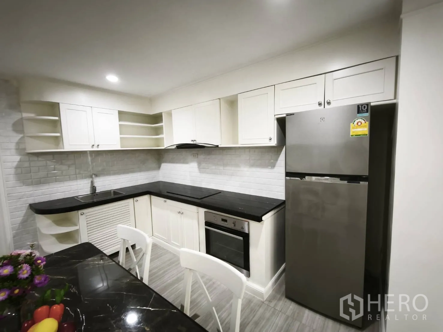 Condominium for rent in Watthana, Bangkok - Corner kitchen featuring oven, cooktop, hood, and a stainless steel refrigerator with white cabinets.