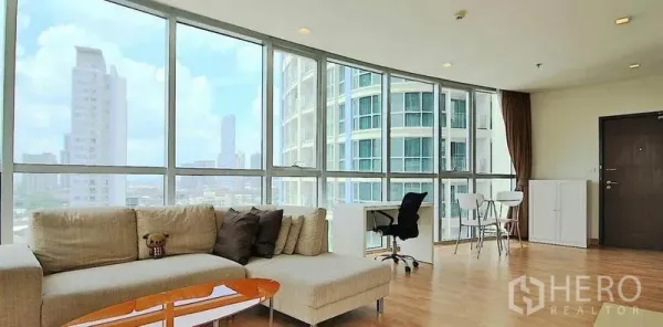 Condominium for rent in Watthana, Bangkok - Corner living room with L-shaped sofa, panoramic windows, work desk and skyline view near BTS Phra Khanong.