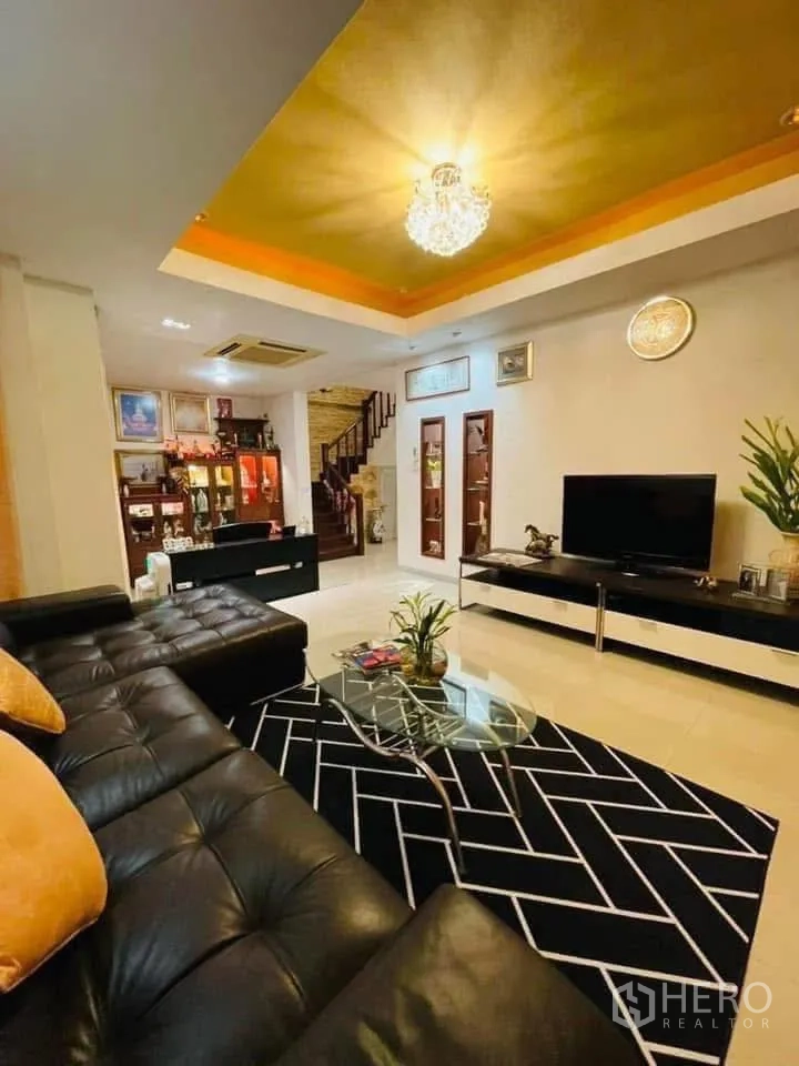 独立式住宅 出租或出售在Lam Luk Ka, Pathum Thani - 宽敞客厅，黑色皮沙发、水晶吊灯与电视柜。