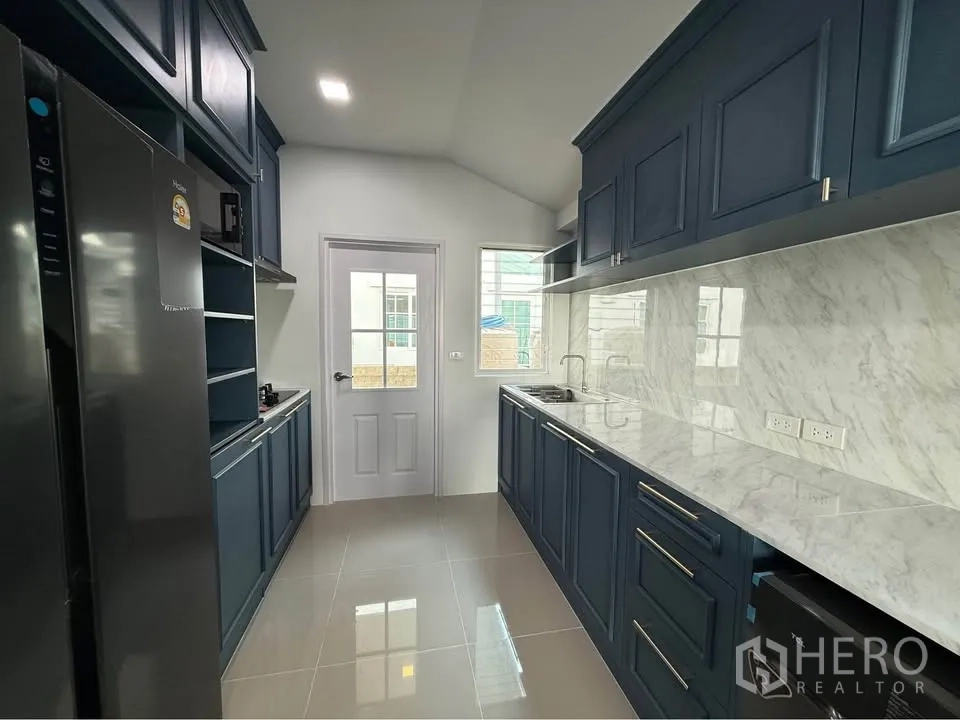 บ้านแฝด for rent in Mueang Samut Prakan, Samut Prakan - ครัวรูปแบบแกลเลอรี่ ตู้สีน้ำเงินเข้ม เคาน์เตอร์ลายหินอ่อน และหน้าต่าง