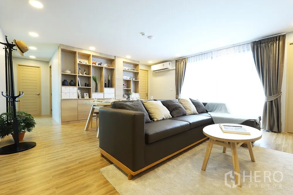Condominium for rent in Watthana, Bangkok - Bright open-plan living room with a large sofa, built-in shelves, dining table and floor-to-ceiling windows.