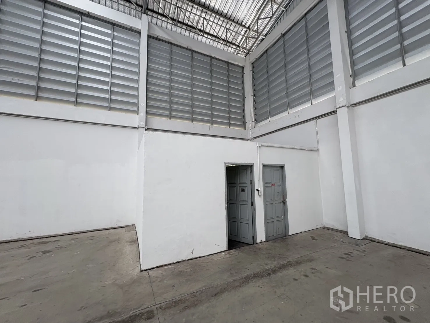 货栈 出租在Ban Phaeo, Samut Sakhon - 仓库一角，通往卫生间的两扇灰色门，墙面上方为通风百叶。