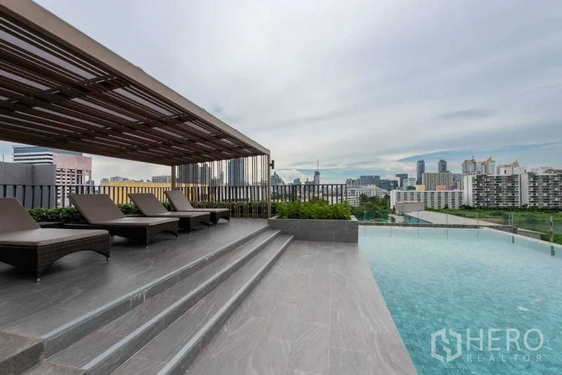Condominium for rent in Huai Khwang, Bangkok - Pool deck with sun loungers under a shaded pergola beside the infinity pool.