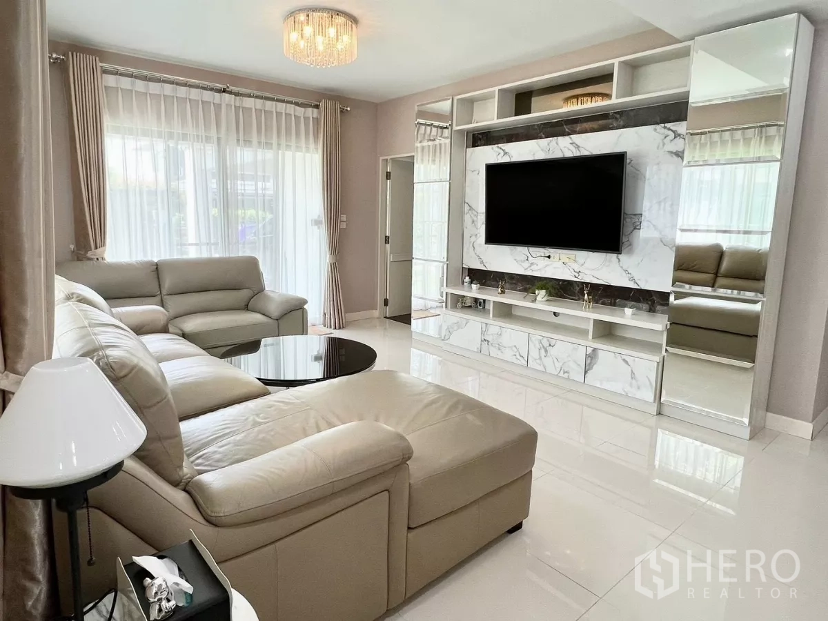 Detached House for rent or sale in Bang Phli, Samut Prakan - Contemporary living room featuring marble TV wall, chandelier lighting and L-shaped sofa.