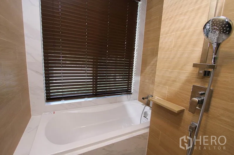 คอนโด ให้เช่าหรือขายในWatthana, Bangkok - ภาพใกล้อ่างอาบน้ำพร้อมฝักบัวมือจับ ผนังลายไม้ และหน้าต่างบานมู่ลี่