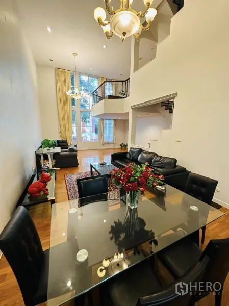 Townhouse for rent in Watthana, Bangkok - Double-height living and dining area with chandelier, floor-to-ceiling windows, mezzanine and black leather sofas.