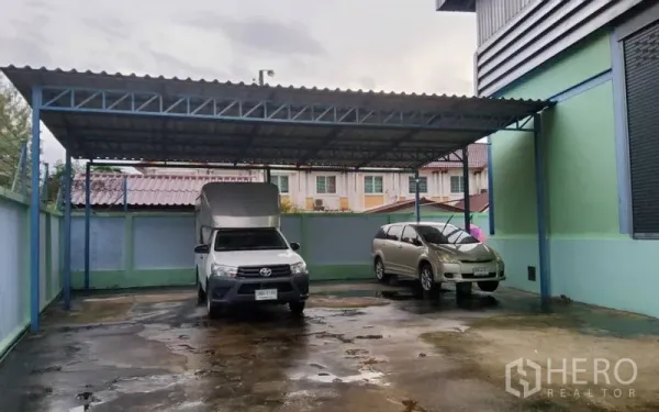 Warehouse for sale in Mueang Nonthaburi, Nonthaburi - Covered parking bay with two vehicles in a gated warehouse compound.