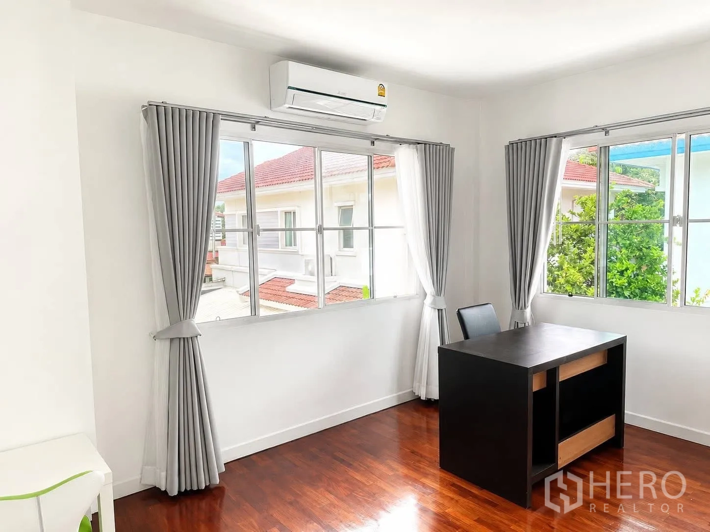 บ้านเดี่ยว for rent in Prawet, Bangkok - มุมห้องทำงานสว่าง มีหน้าต่างบานใหญ่ ม่านสีเทา เครื่องปรับอากาศ และโต๊ะสีดำบนพื้นไม้