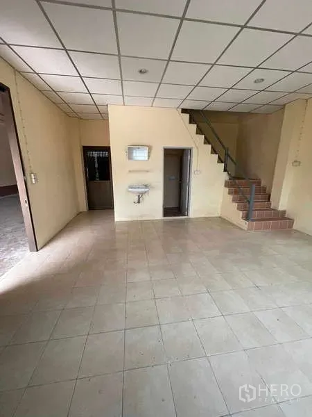 Warehouse for rent in Bang Bua Thong, Nonthaburi - Ground-floor office area with tiled floor, staircase to upper level and access to bathroom.