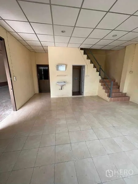 Warehouse for rent in Bang Bua Thong, Nonthaburi - Ground-floor office area with tiled floor, staircase to upper level and access to bathroom.