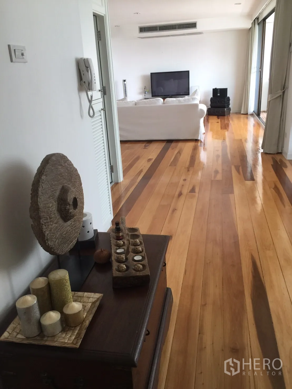 Condominium for rent in Watthana, Bangkok - Hallway with glossy wooden flooring leading to a TV lounge with white sofa and access to the balcony.