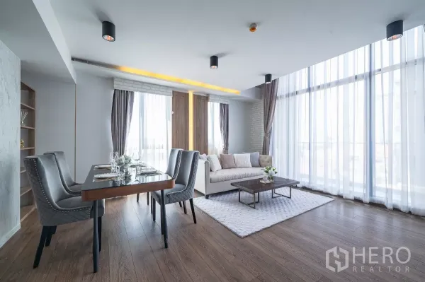 Condominium for rent or sale in Phra Khanong, Bangkok - Bright open-plan living and dining area with floor-to-ceiling sheer curtains, wood flooring, and a modern sofa set.