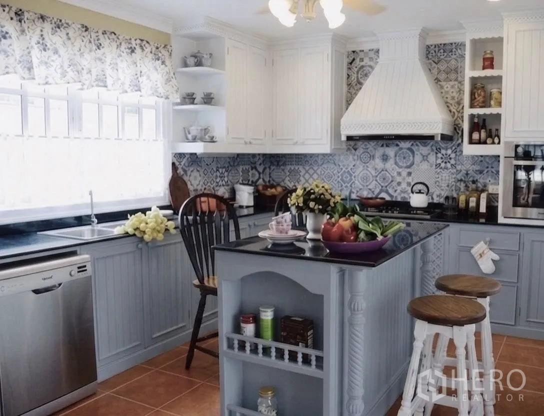 Detached House for rent in Mueang Samut Prakan, Samut Prakan - Bright country-style kitchen with island, patterned backsplash, white cabinets and stools.