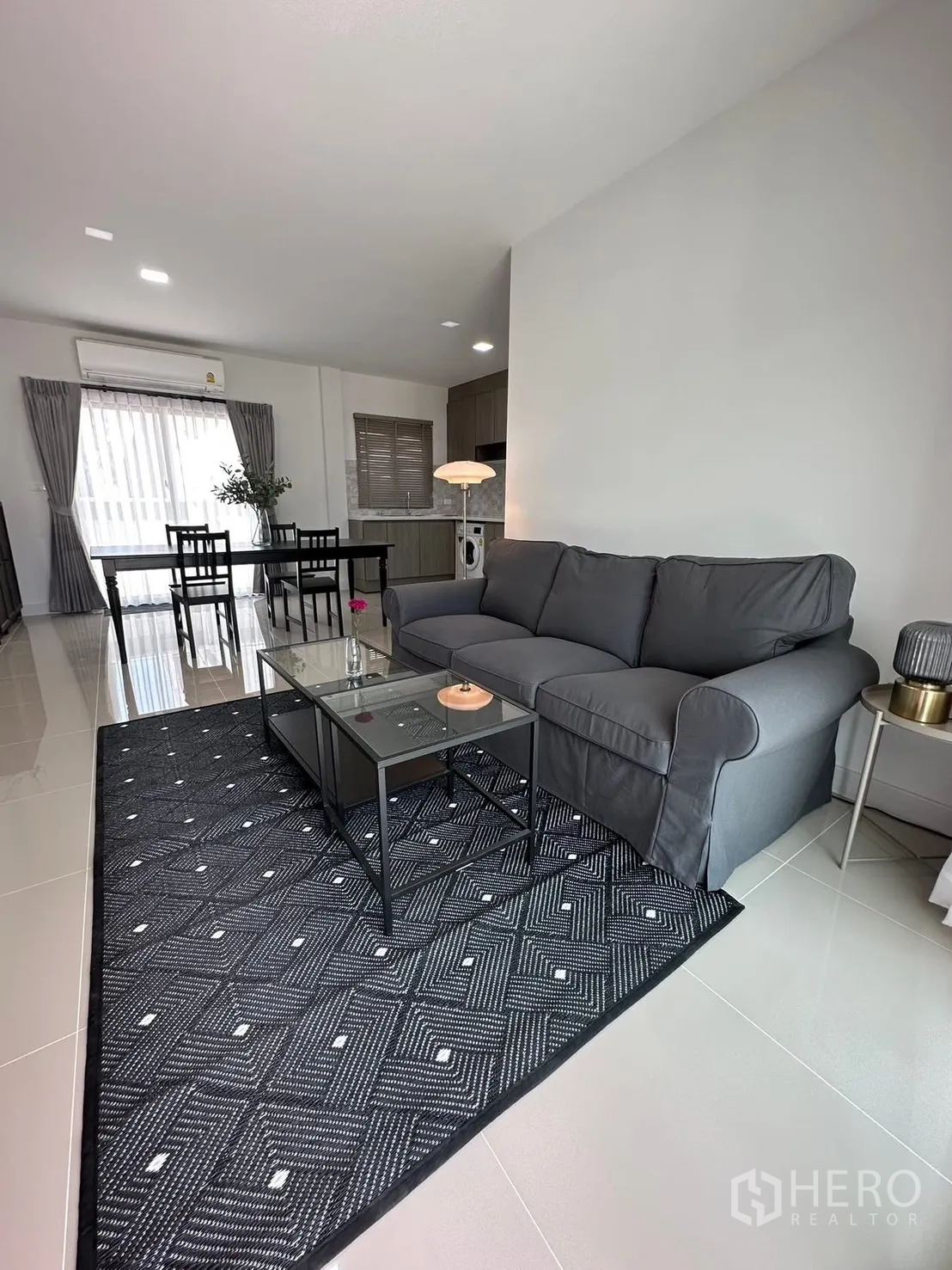 Townhouse for rent in Bang Phli, Samut Prakan - Open-plan living room with gray sofa, glass coffee table, and dining area.