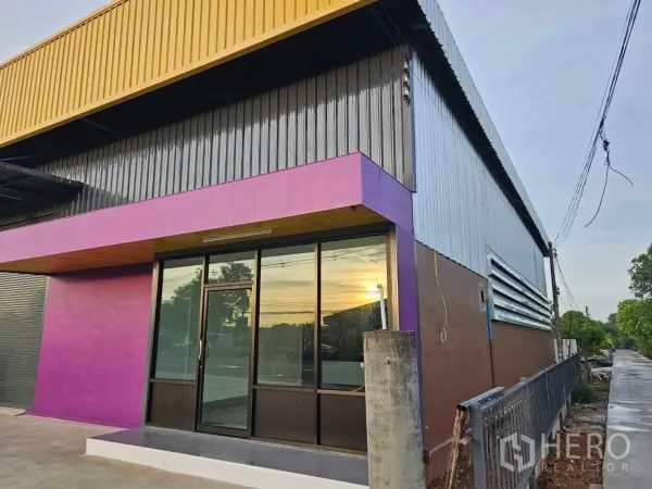 คลังสินค้า ให้เช่าในLam Luk Ka, Pathum Thani - มุมอาคารด้านข้างโชว์ทางเข้าออฟฟิศกระจกใส ใต้แผงหลังคาสีเหลืองและแถบสีม่วง