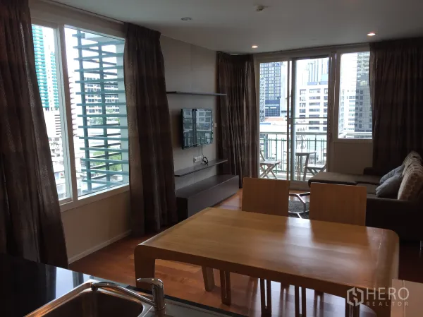 คอนโด ให้เช่าหรือขายในWatthana, Bangkok - ห้องนั่งเล่นสว่าง ทีวีติดผนัง โซฟามุม และระเบียงชมวิวสกายไลน์กรุงเทพฯ