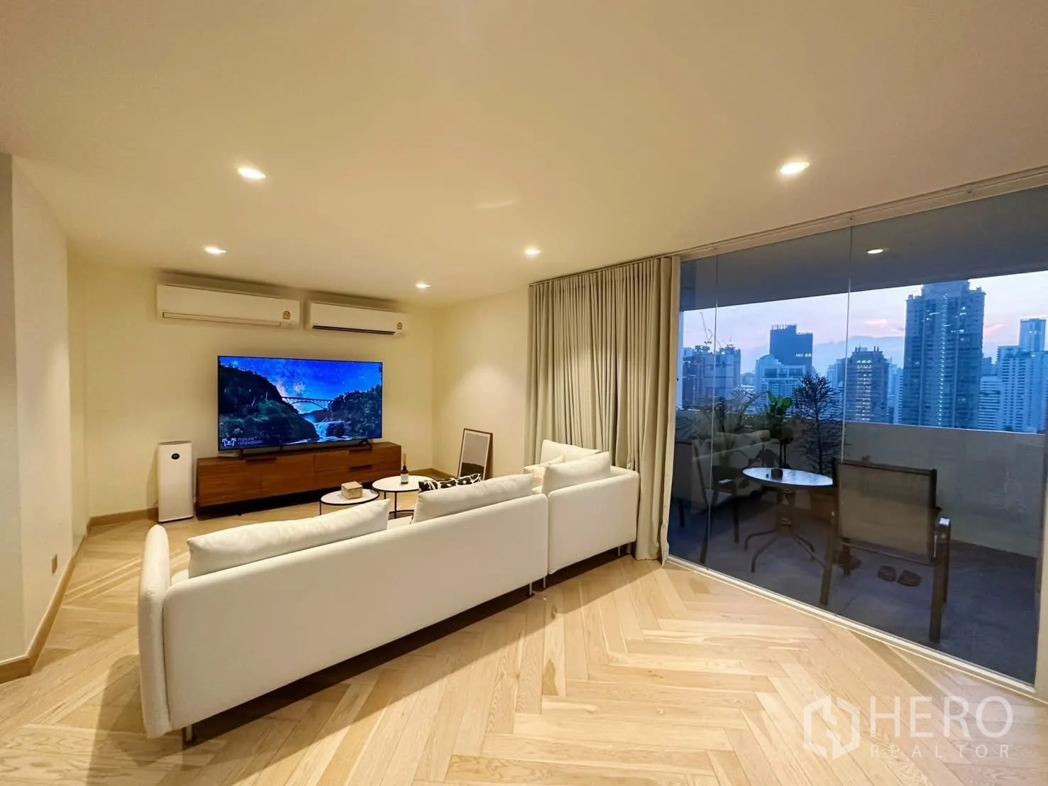 Condominium for rent or sale in Watthana, Bangkok - Living room with white sofa, large TV, and floor-to-ceiling glass wall.