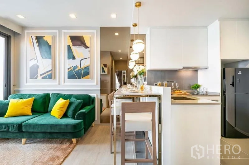 Condominium for rent or sale in Watthana, Bangkok - Open-plan living and dining with green sofa, breakfast bar and pendant lights beside a white kitchen.