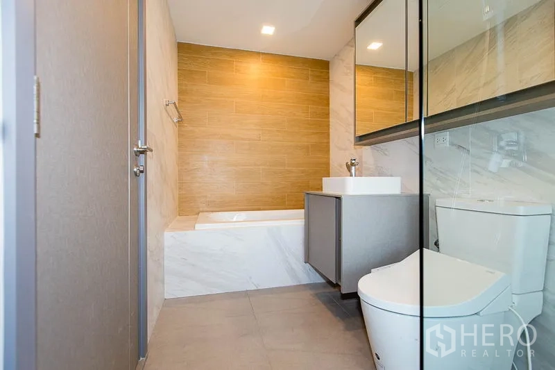 Condominium for rent in Watthana, Bangkok - Second bathroom featuring a built-in bathtub, wood accent wall, vanity and toilet.