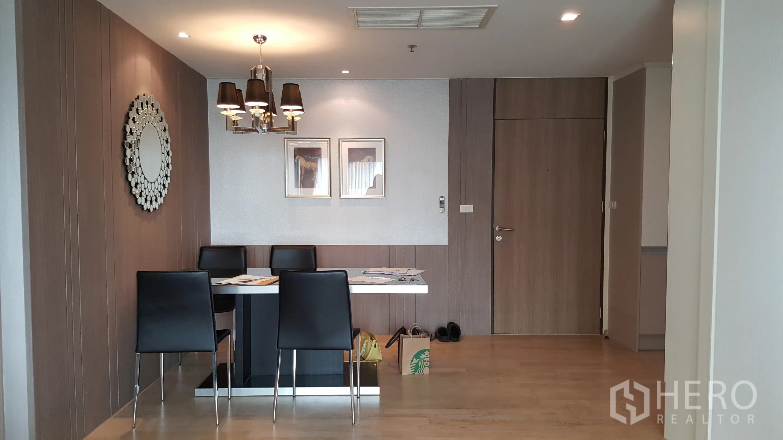 Condominium for rent in Khlong Toei, Bangkok - Dining area with four-seat table, chandelier lighting and wood-paneled feature wall.