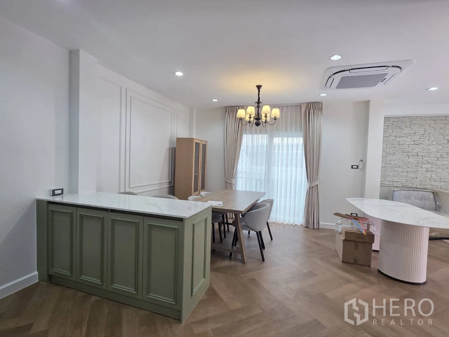 Detached House for sale in Lam Luk Ka, Pathum Thani - Open-plan living and dining with cassette ceiling air-con, stone accent wall, and marble peninsula.
