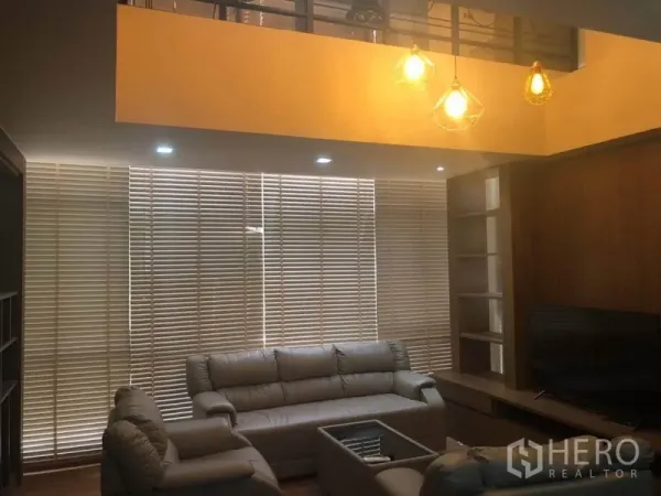 คอนโด ขายในBang Na, Bangkok - ห้องนั่งเล่นเพดานสูง โคมไฟห้อย โซฟาหนัง ตู้วางทีวี และมู่ลี่เต็มผนัง