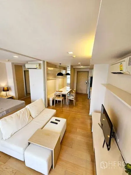 Condominium for rent - Bright living room with white sofa, TV shelf and dining table in a modern Bangkok condo.