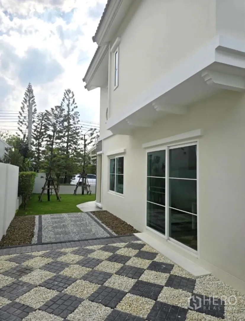 Detached House for rent in Bang Phli, Samut Prakan - Side yard with patterned stone walkway beside the white exterior wall.