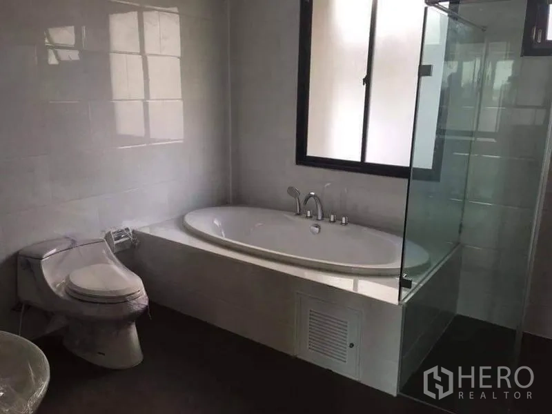 Townhouse for sale in Yan Nawa, Bangkok - Modern bathroom featuring a soaking bathtub, separate glass shower enclosure and window.