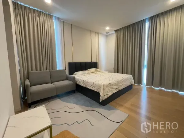 Detached House for rent in Bueng Kum, Bangkok - Bright bedroom with king bed, grey sofa, full-height curtains and timber floors.