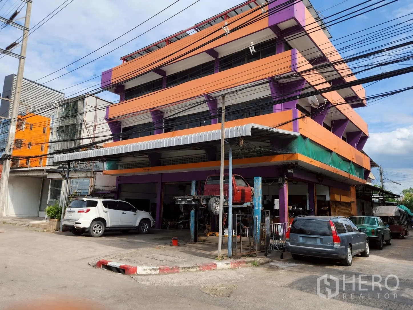 อาคาร standalone for rent or sale in Mueang Pathum Thani, Pathum Thani - ภาพมุมตึกอาคารเดี่ยวพร้อมชายคาหน้าร้านและรถจอดหลายคัน