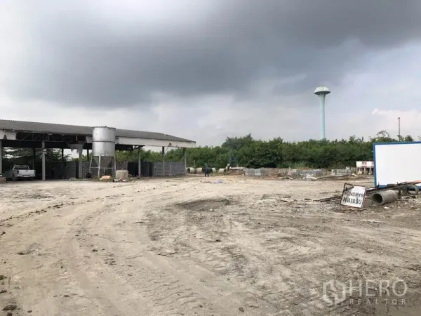 工厂 出租在Phra Nakhon Si Ayutthaya - 棚旁广阔作业场地，远处可见高塔水塔与物料堆。