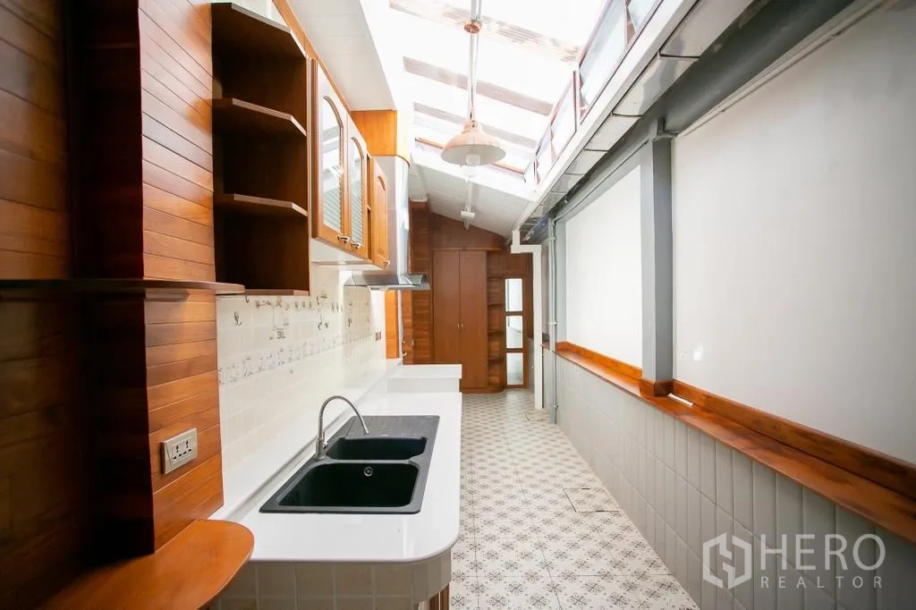 Detached House for rent or sale in Huai Khwang, Bangkok - Bright galley kitchen with skylight, white countertops and dual black sinks.