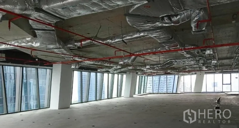 Office Space for rent - Shell-and-core office floor with exposed ducts, red sprinkler pipes and full-height windows overlooking the Bangkok skyline.