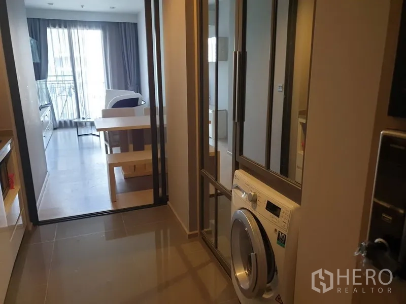 Condominium for rent in Watthana, Bangkok - Entry hall with mirrored closets and a front-loading washing machine leading to a bright living room and balcony.