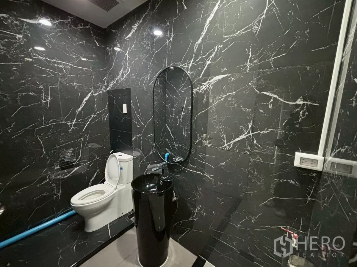 Condominium for sale in Bang Kho Laem, Bangkok - Spacious bathroom with black marble walls, glass shower and a white toilet.
