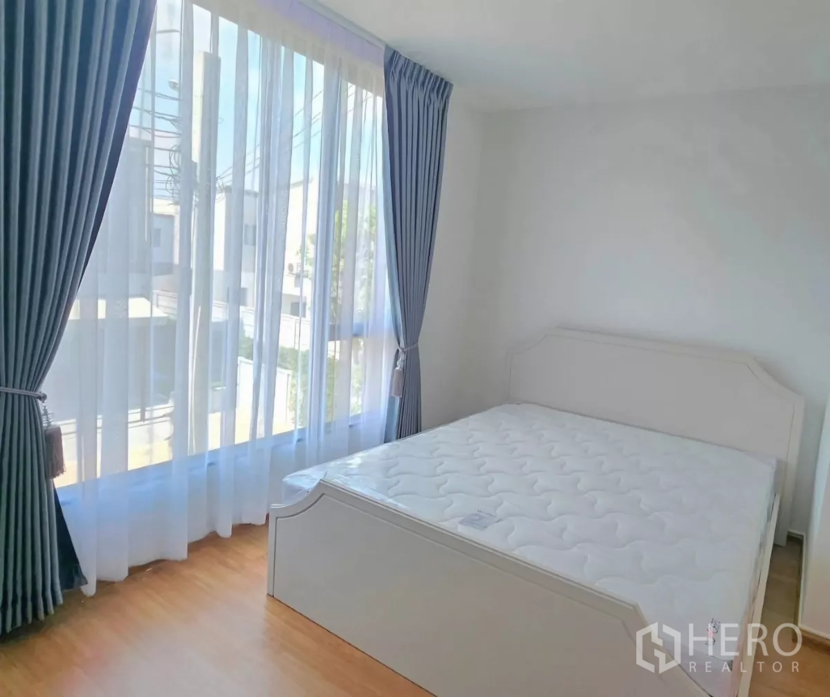 ทาวน์เฮาส์ ให้เช่าในBang Phli, Samut Prakan - ห้องนอนสว่าง พร้อมหน้าต่างสูง ผ้าม่านสีน้ำเงิน และเตียงสีขาวพื้นไม้