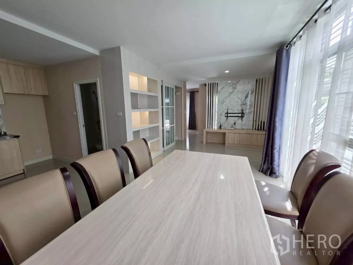 Detached House for rent or sale in Samut Prakan - Dining space beside large curtained windows and a marble TV feature wall.