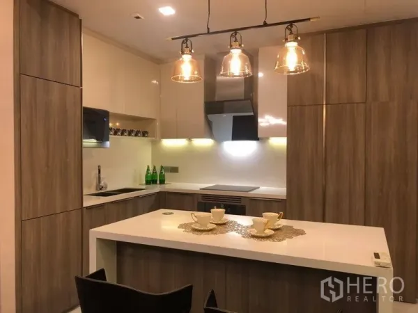 Condominium for rent in Watthana, Bangkok - L-shaped contemporary kitchen with wood cabinetry, white countertops and integrated appliances.