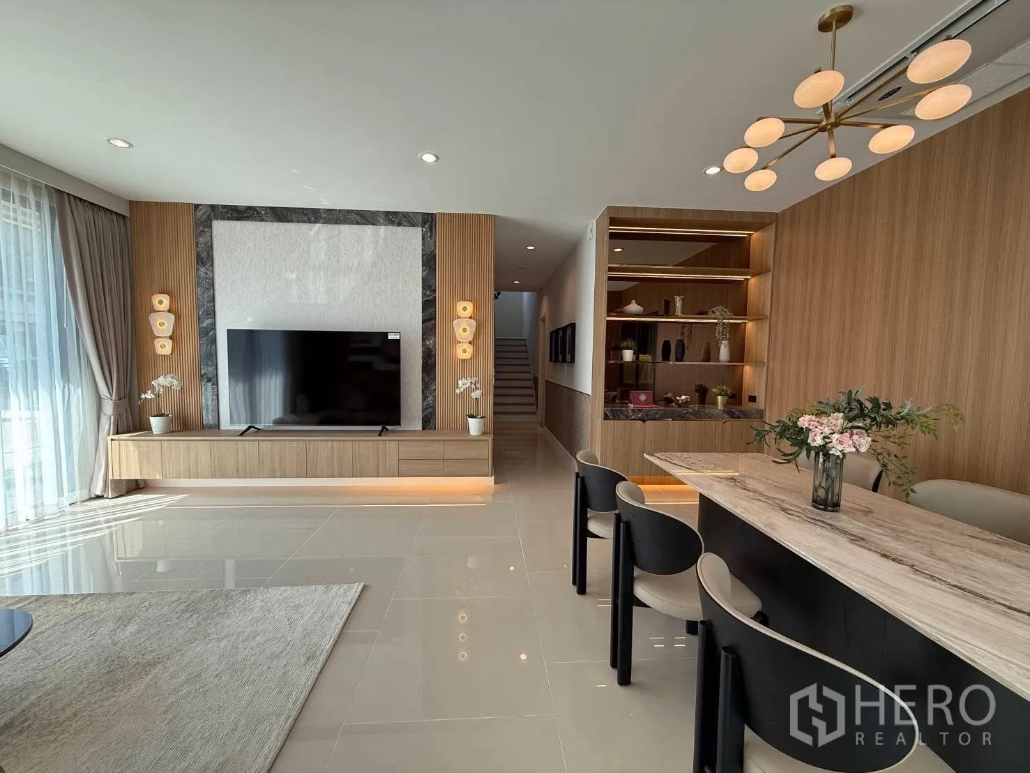 Detached House for rent in Bang Phli, Samut Prakan - Living room showcasing a TV on a feature wall, built-in console, shelves, and dining area lighting.