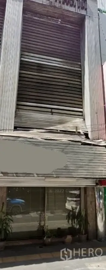 อาคารพาณิชย์ ให้เช่าในKhlong Toei, Bangkok - อาคารพาณิชย์หลายชั้น ด้านหน้ากระจกชั้นล่าง ประตูม้วนโลหะ และกระถางต้นไม้ ใกล้ BTS ทองหล่อ ในกรุงเทพฯ