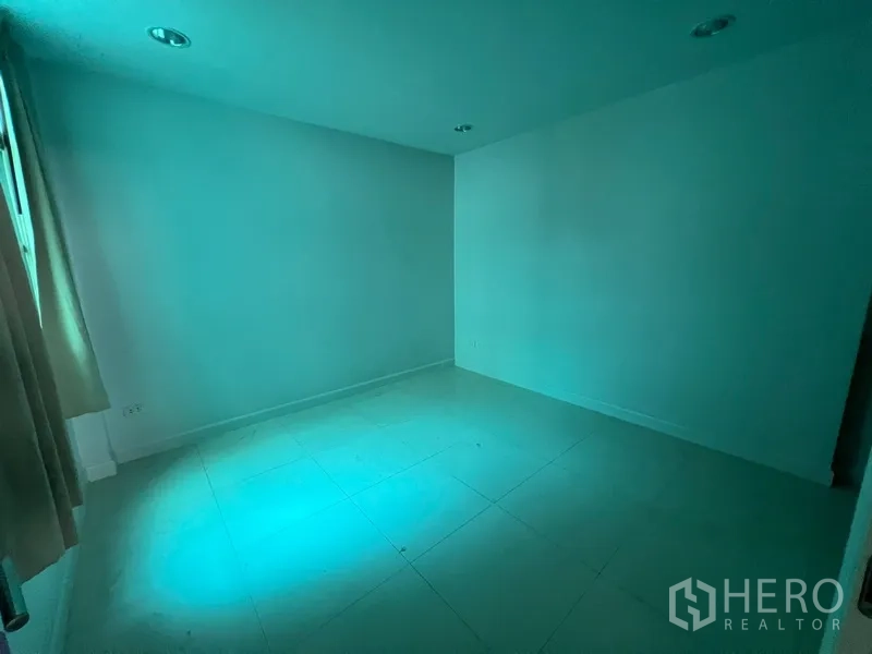 Townhouse for rent in Din Daeng, Bangkok - Empty room with tiled floor and blue-tinted lighting from window.