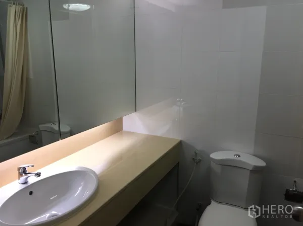 Condominium for rent in Watthana, Bangkok - Modern bathroom with large mirror, long countertop, toilet, and bathtub with curtain.