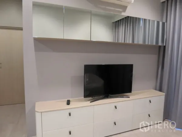 Condominium for rent in Watthana, Bangkok - Living room media wall featuring a flat-screen TV on a white storage cabinet with mirrored overhead cupboards.