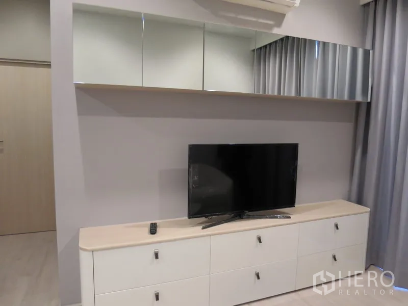 Condominium for rent in Watthana, Bangkok - Living room media wall featuring a flat-screen TV on a white storage cabinet with mirrored overhead cupboards.
