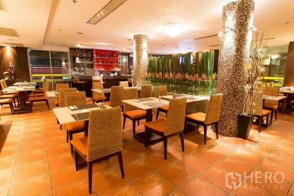 零售空间 出租在Khlong Toei, Bangkok - 餐厅内部朝向吧台，绿植隔断与橙色座椅。