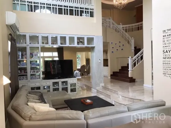 独立式住宅 出租 - 挑高客厅，L 型沙发、吊灯、电视墙柜以及带白色栏杆的弧形楼梯。