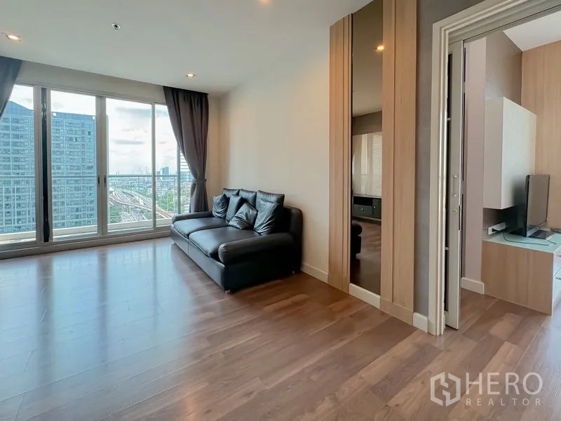 คอนโด ขาย - มุมนั่งเล่นโซฟาหนังสีดำข้างหน้าต่างบานใหญ่และระเบียง